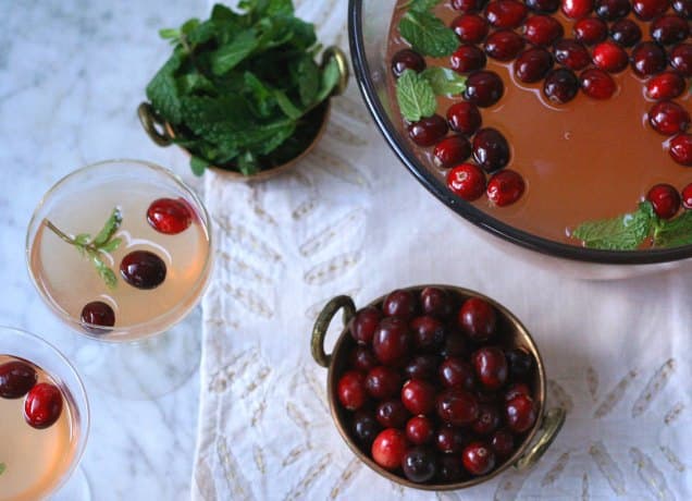 holiday punch bowl cocktails: cranberry mint cocktail in a bowl with two glasses and a bowl of cranberries