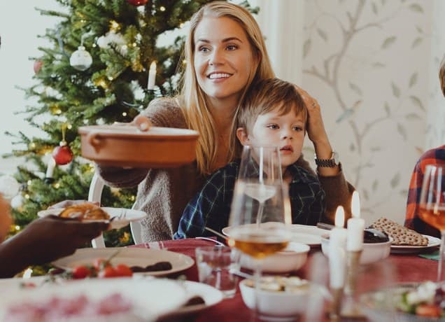 A mom holding a child in front of christmas tree passes a tray around