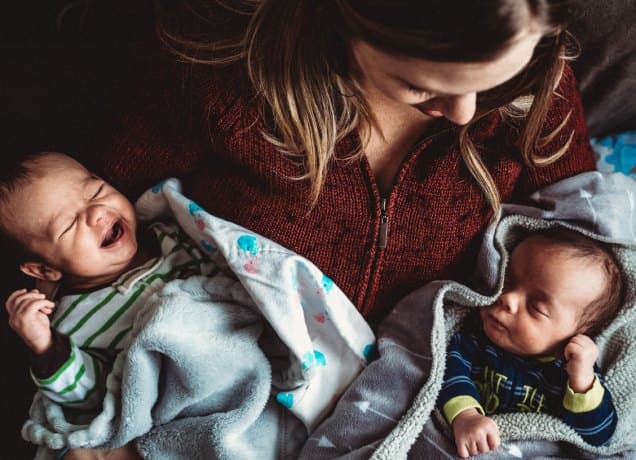 who-is-older-birth-order-question-for-twins: A mother holds twin babies in her hands while she looks at them fondly.